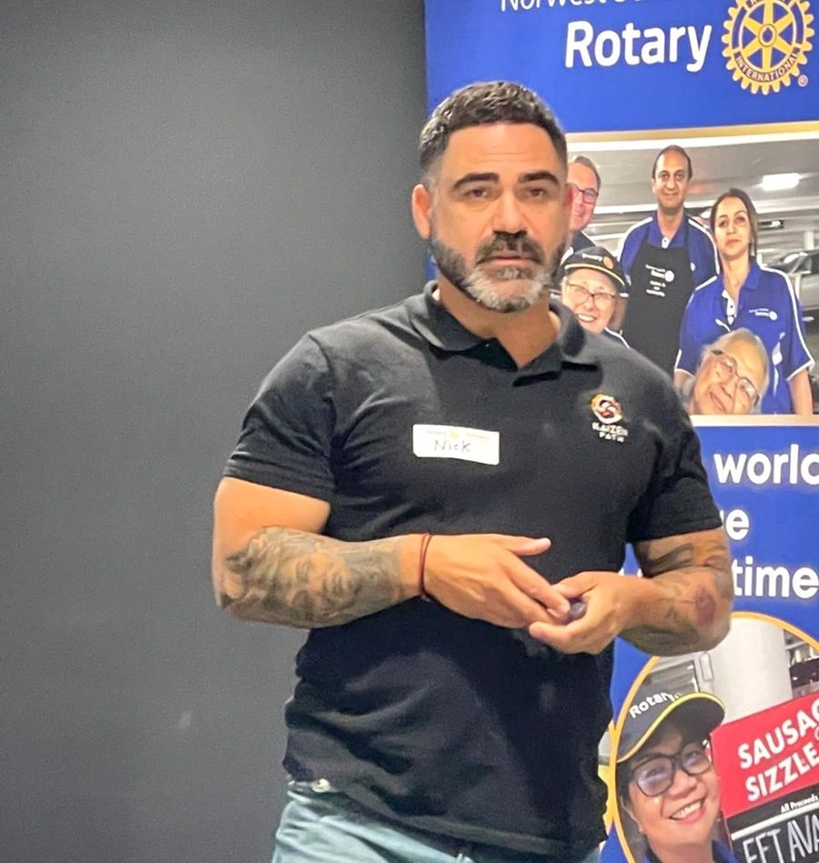 Nick Stamatis speaking beside a Norwest Sunrise Rotary Club banner